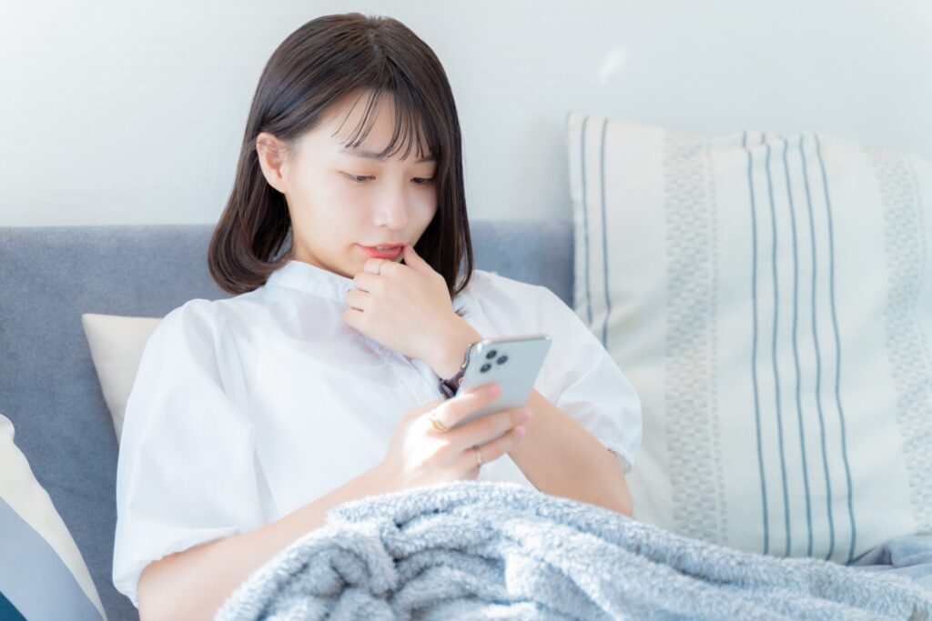 親指を口に当ててスマホを見る女性