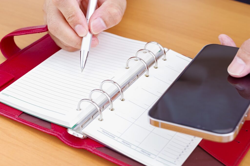 スマホを見ながら手帳を書き込む人の手元