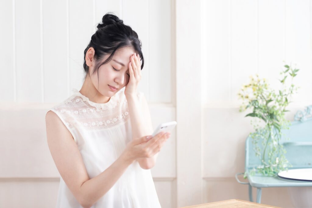 スマホを見て悩む女性（体調不良）