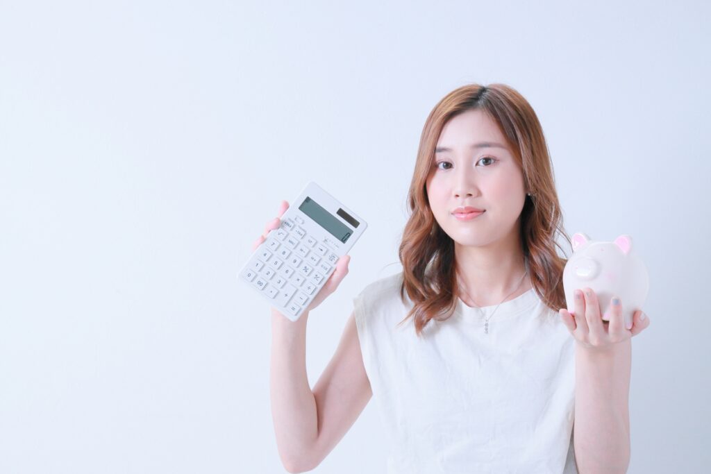 計算機と貯金箱を持ったＴシャツ姿の女性